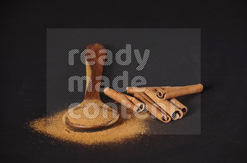 Cinnamon powder in a wooden ladle spoon with cinnamon sticks on black background