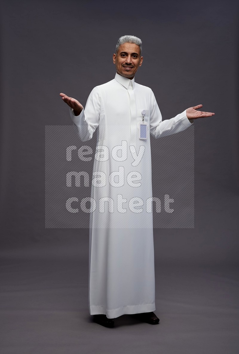 Saudi man wearing thob with pocket employee badge standing interacting with the camera on gray background