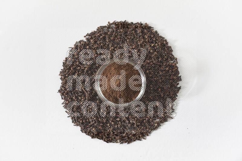A glass bowl full of cloves powder and cloves grains spread on white flooring
