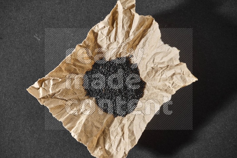 A crumpled piece of paper full of black seeds on a black flooring in different angles