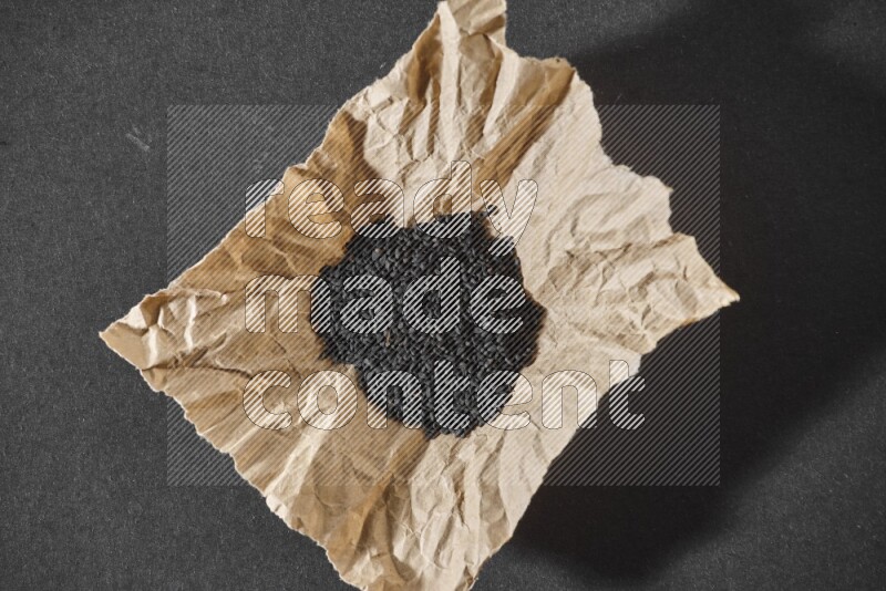 A crumpled piece of paper full of black seeds on a black flooring