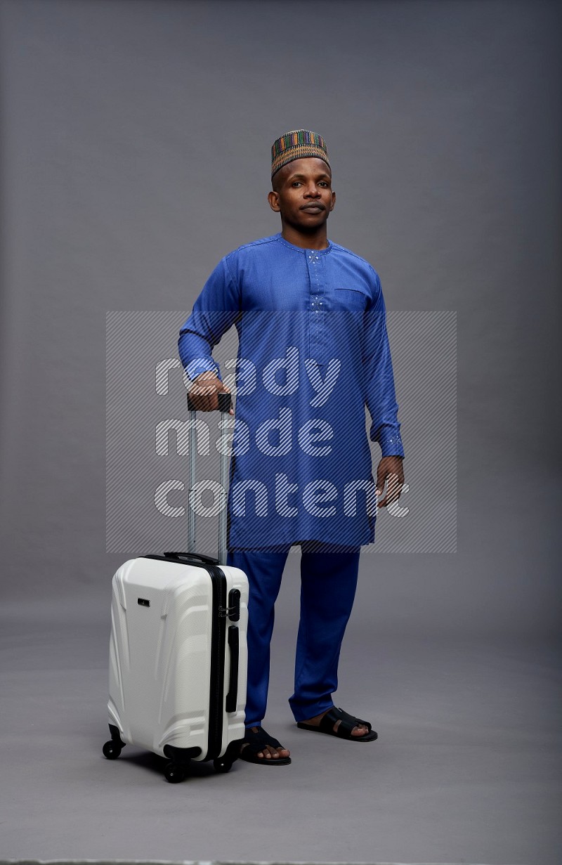 Man wearing Nigerian outfit standing holding bag on gray background