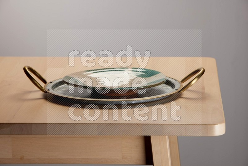 multicolored plate placed on a rounded stainless steel tray with golden handels on the edge of wooden table