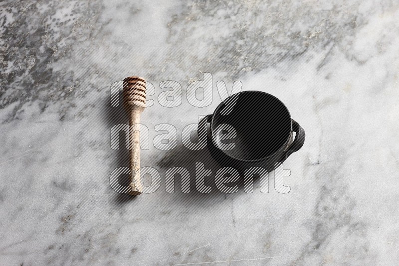 Black Pottery bowl with wooden honey handle on the side with grey marble flooring, 65 degree angle
