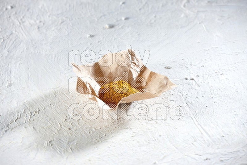 Turmeric powder in a crumpled piece of paper on textured white flooring