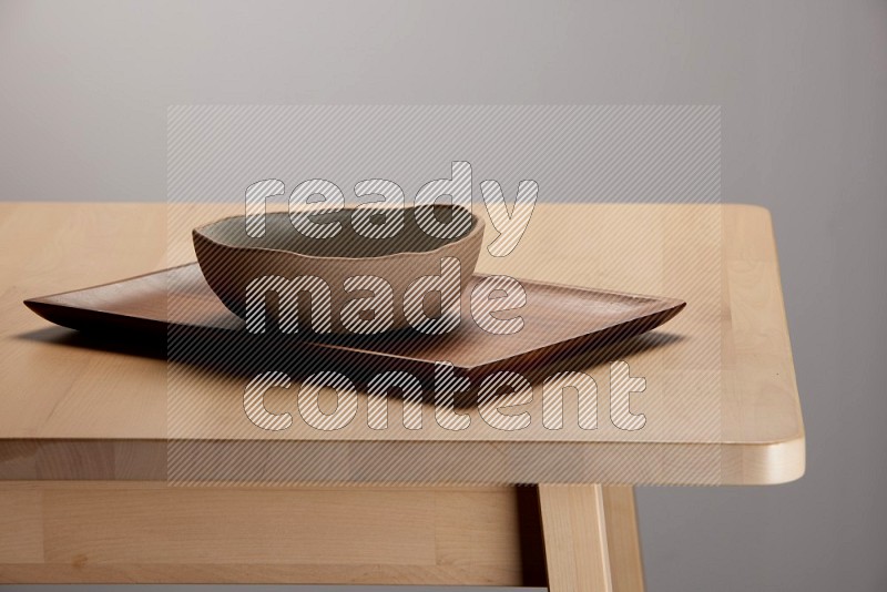 multicolored bowl placed on a rectangular wooden tray on the edge of wooden table