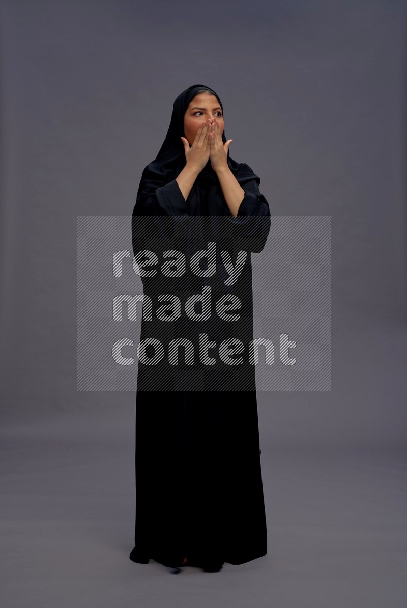 Saudi woman wearing Abaya standing hands behind head on gray background