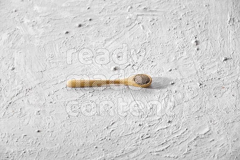 A wooden spoon full of black pepper powder on a textured white flooring