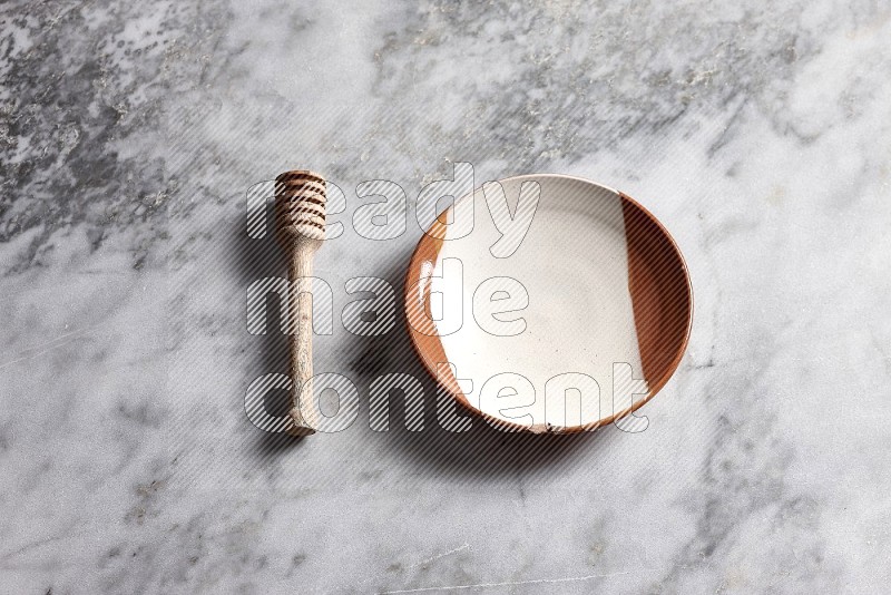 Multicolored Pottery Plate with wooden honey handle on the side with grey marble flooring, 65 degree angle