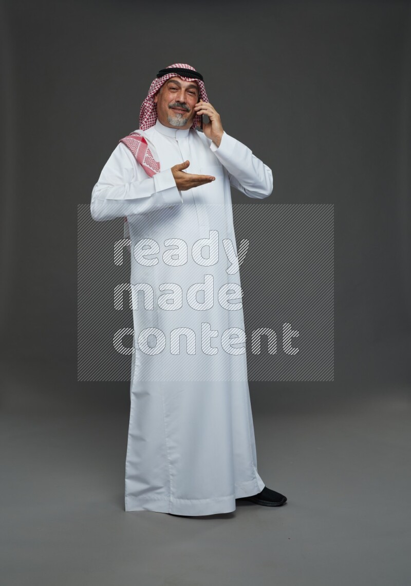Saudi man with shomag Standing talking on phone on gray background