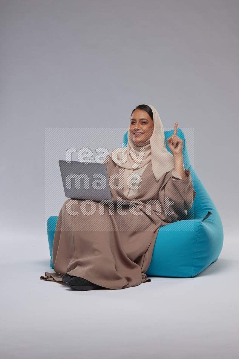 A Saudi woman sitting on a blue beanbag and working on laptop