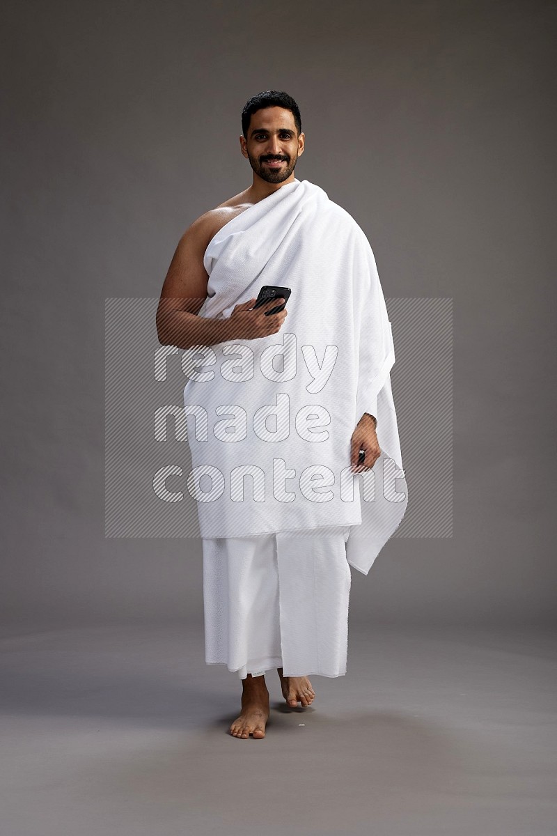 A man wearing Ehram Standing texting on phone on gray background