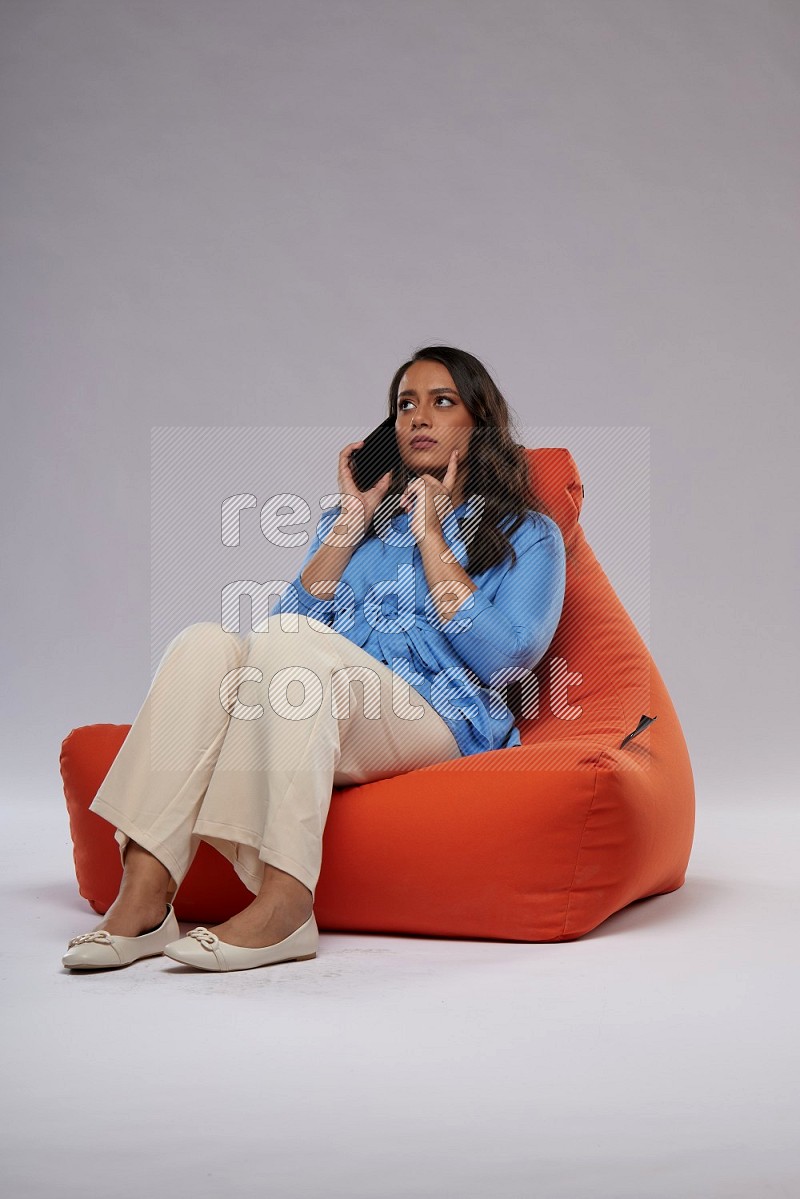 A woman sitting on an orange beanbag and talking on the phone