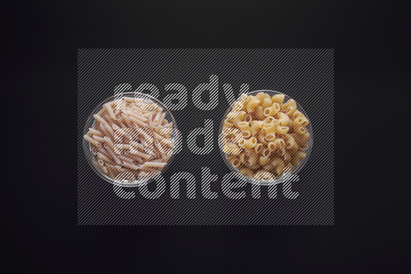 Different pasta types in glass bowls on black background