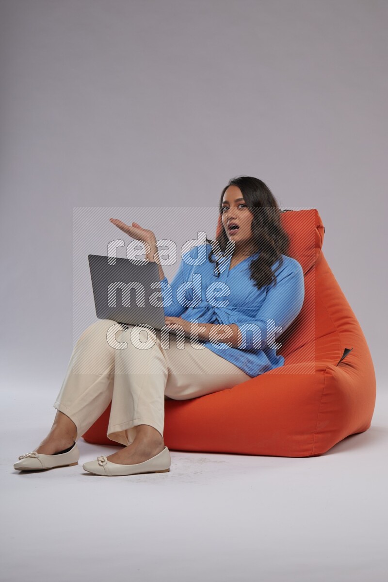 A woman sitting on an orange beanbag and working on laptop