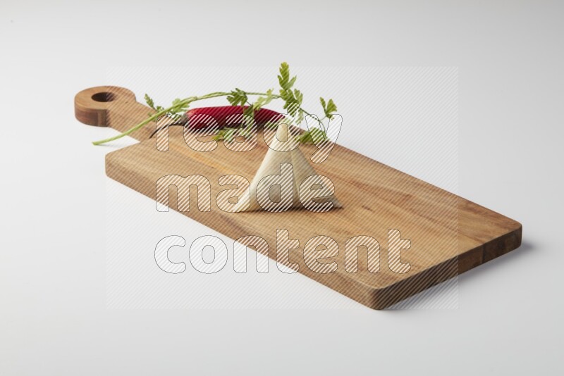 One uncooked samosa with a single red pepper and parsley on a wooden cutter on a white background