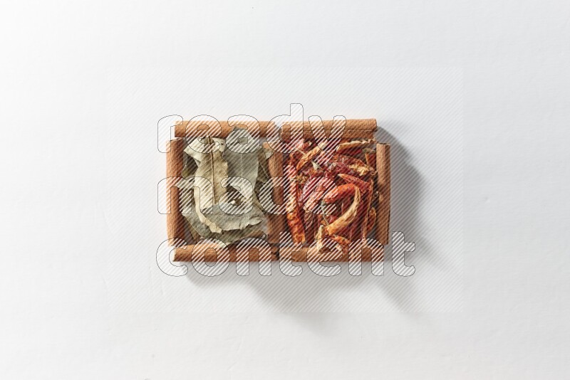 مربعان من أعواد القرفة ممتلئان بالفلفل الحار المجفف وأوراق الغار علي خلفية بيضاء