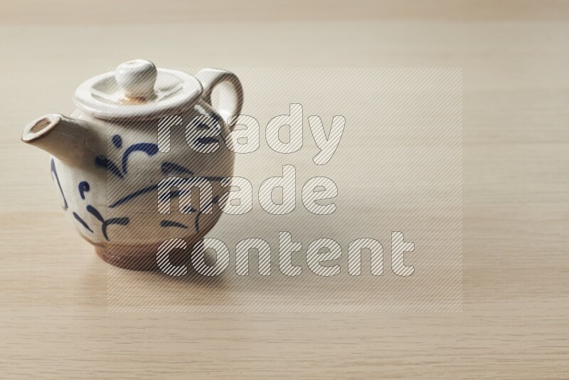 A pottery teapot on light wooden background