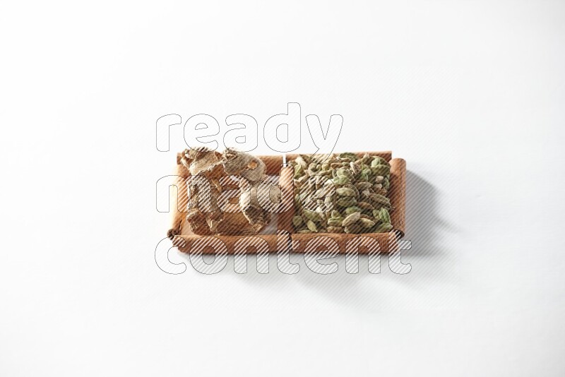 مربعان من أعواد القرفة ممتلئان بحبوب الهيل والزنجبيل المجفف علي خلفية بيضاء