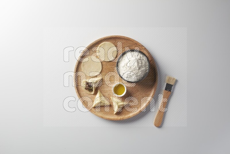 two closed sambosas and one open sambosa filled with meat while flour, and oil with oil brush aside in a wooden dish on a white background