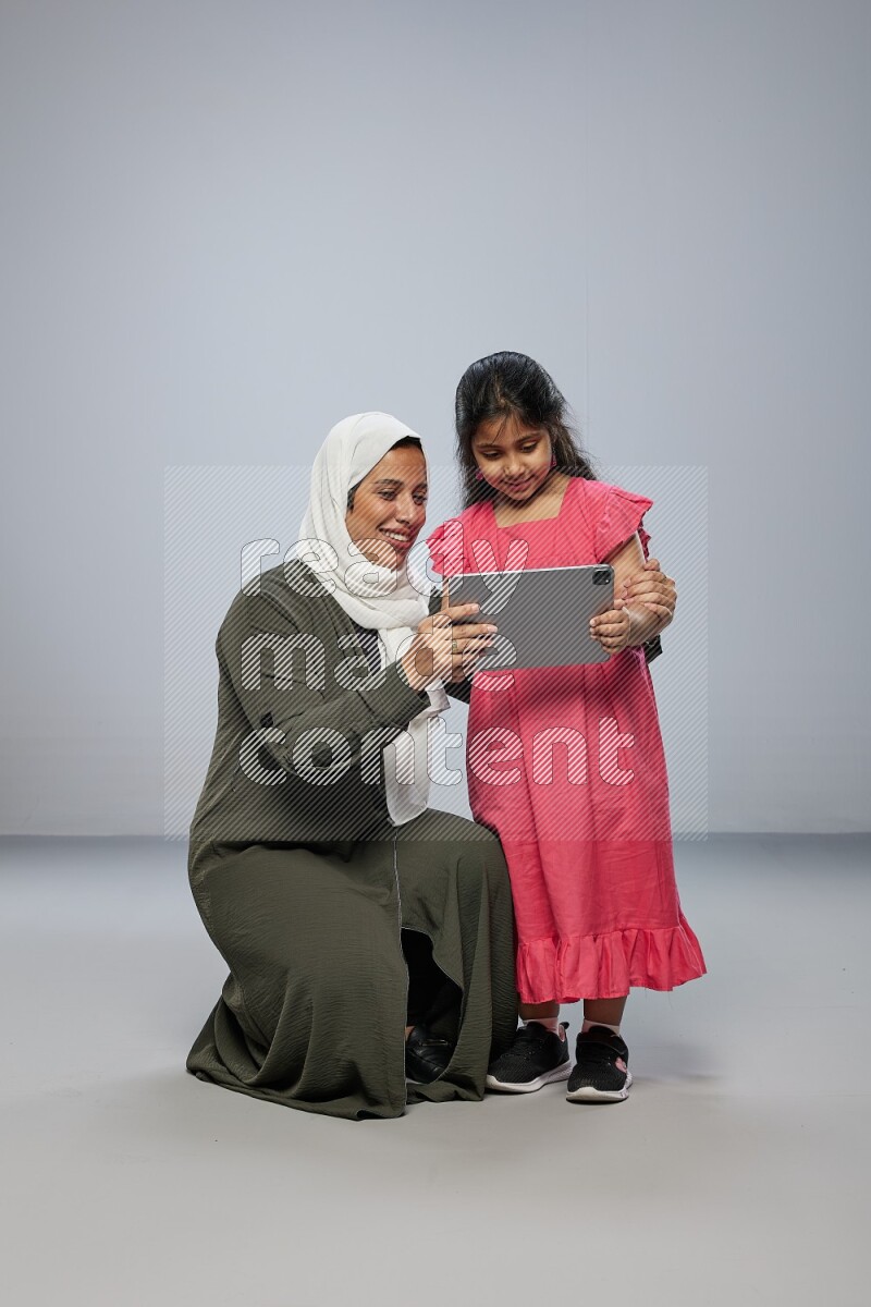 A girl holding an Ipad with her mother on gray background