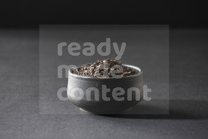 A black pottery bowl full of cloves on a black flooring