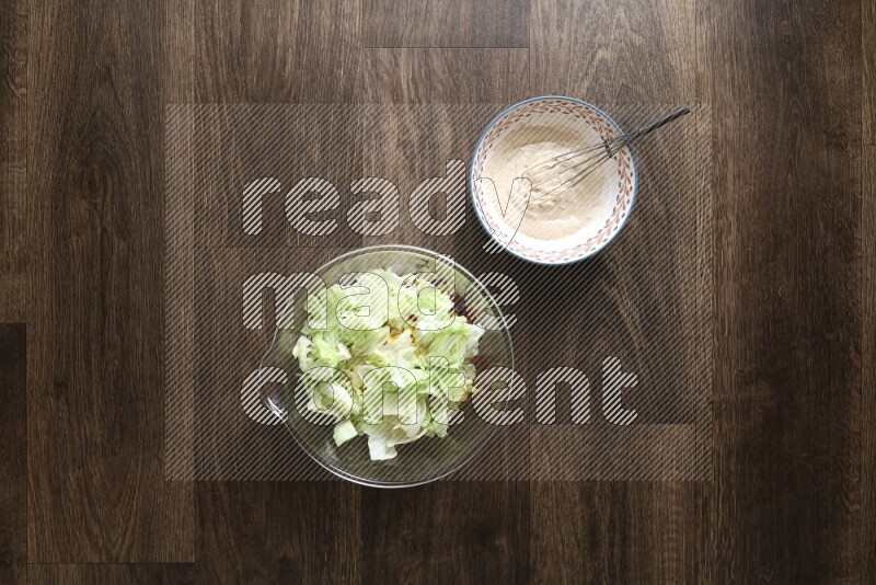 A bowl full of salad (avocado, tomatoes, red beans, olives, bell pepper, corn, lettuce) and bowl of salad dressing on wooden background