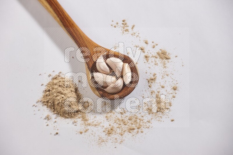 A wooden ladle full of garlic cloves with sprinkled powder on a white flooring