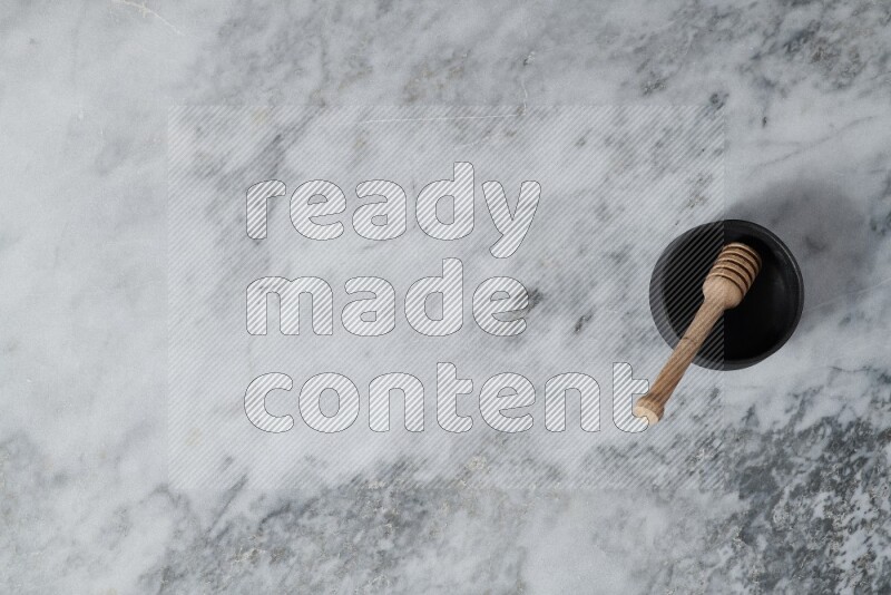 وعاء فخاري أسود مع ملعقة عسل خشبية بداخله على خلفية من الرخام الرمادي