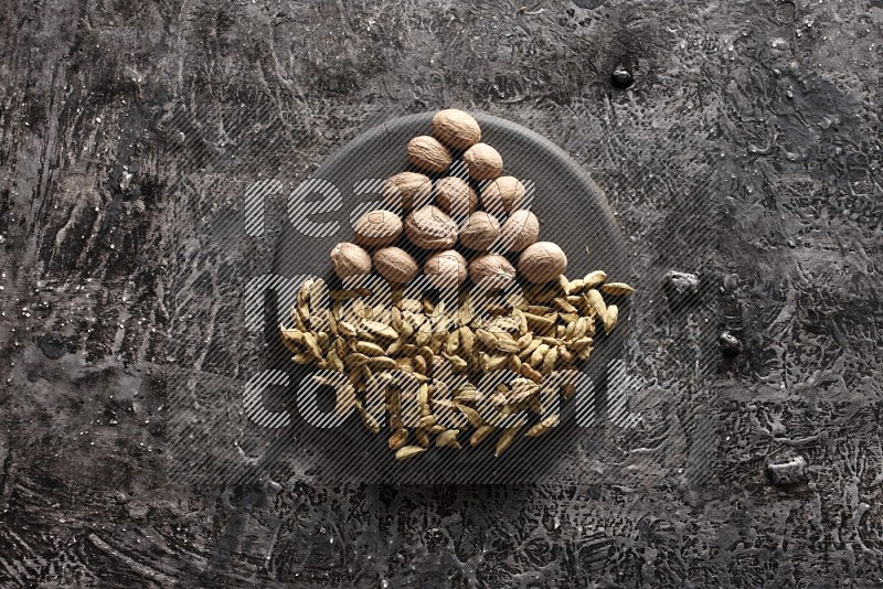 Cardamom and nutmeg on a black plate on textured black background