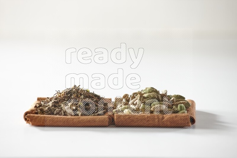 2 squares of cinnamon sticks full of cardamom and dried basil on white flooring