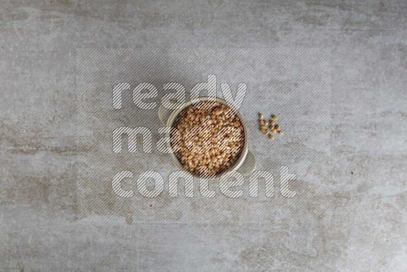 corn kernel in a off-white handheld ceramic bowl on a grey textured countertop