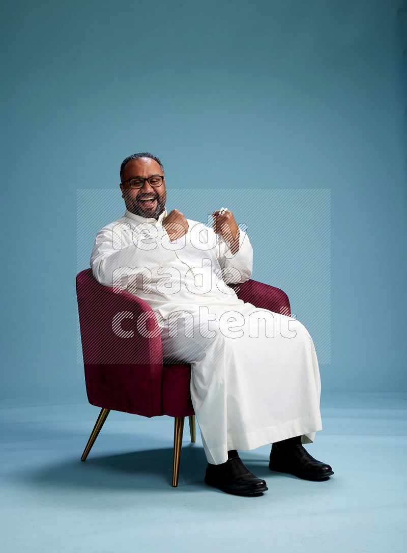 Saudi Man without shimag sitting on chair Interacting with the camera on blue background