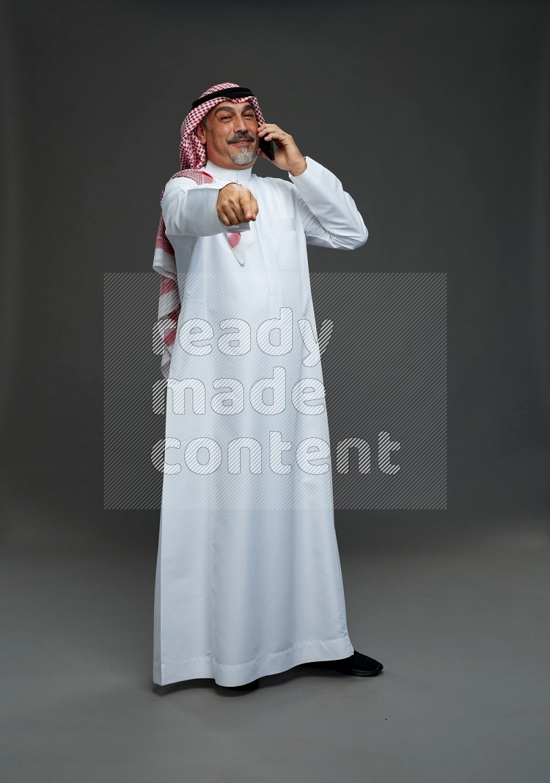 Saudi man with shomag Standing talking on phone on gray background