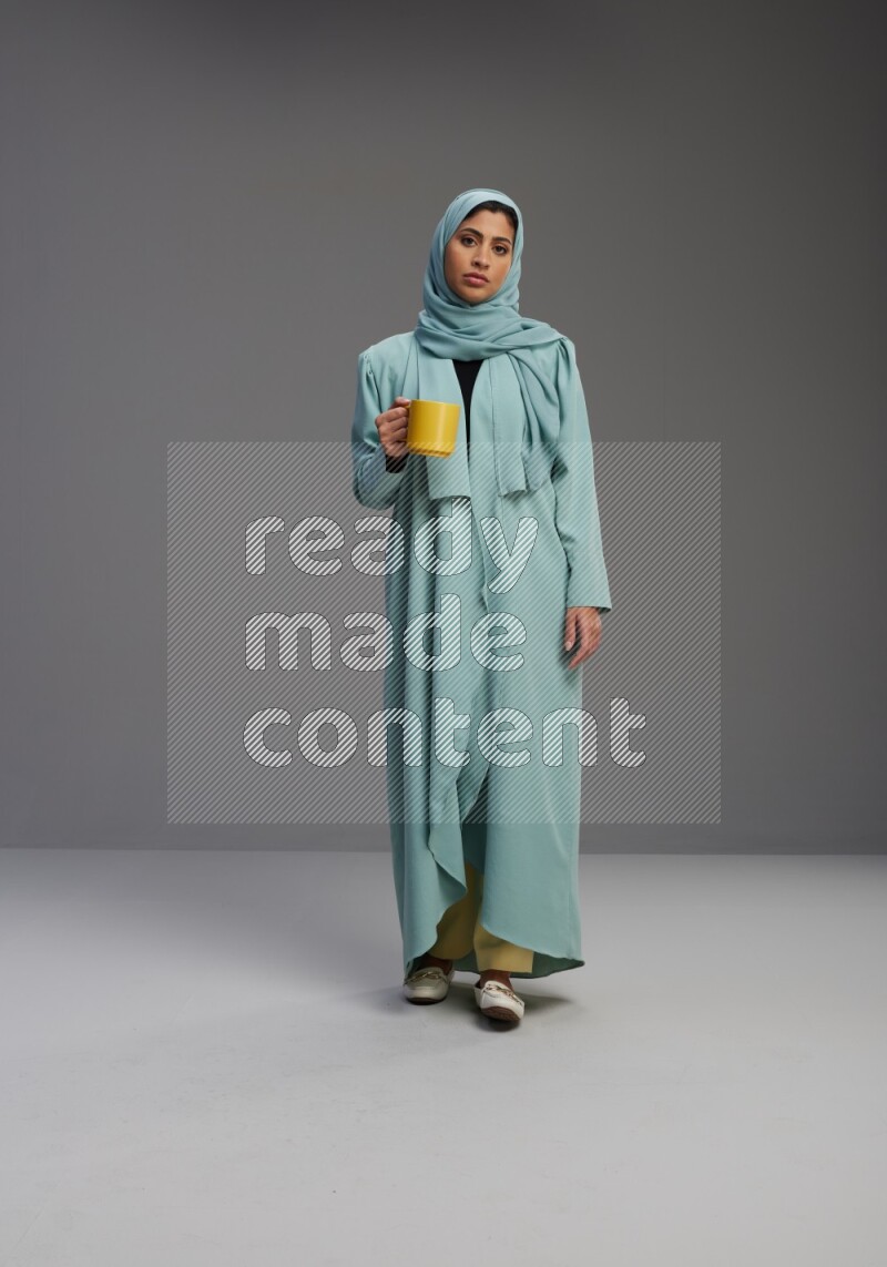 Saudi Woman wearing Abaya standing  holding a mug on Gray background