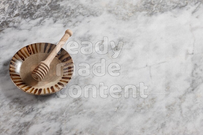 Multicolored pottery plate with wooden honey dipper in it on grey marble background