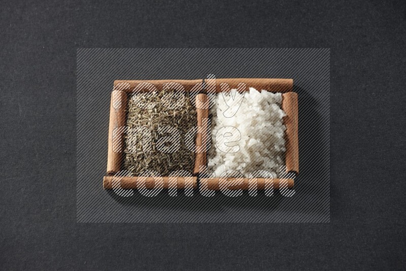 2 squares of cinnamon sticks full of white salt and cumin on black flooring