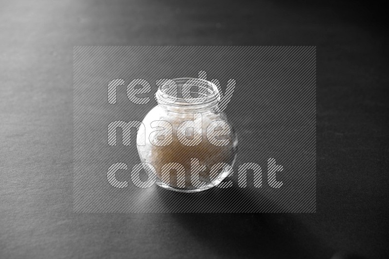 A glass spice jar full of salt on black flooring