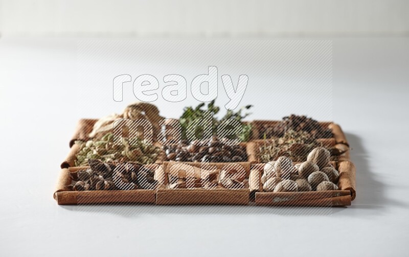 9 مربعات من أعواد القرفة ممتلئة بحبوب القهوة في المنتصف محاطة بالنعناع المجفف والزنجبيل المجفف وحبوب الهيل واليانسون النجمي والقرفة وجوزة الطيب والريحان المجفف والقرنفل على أرضية بيضاء