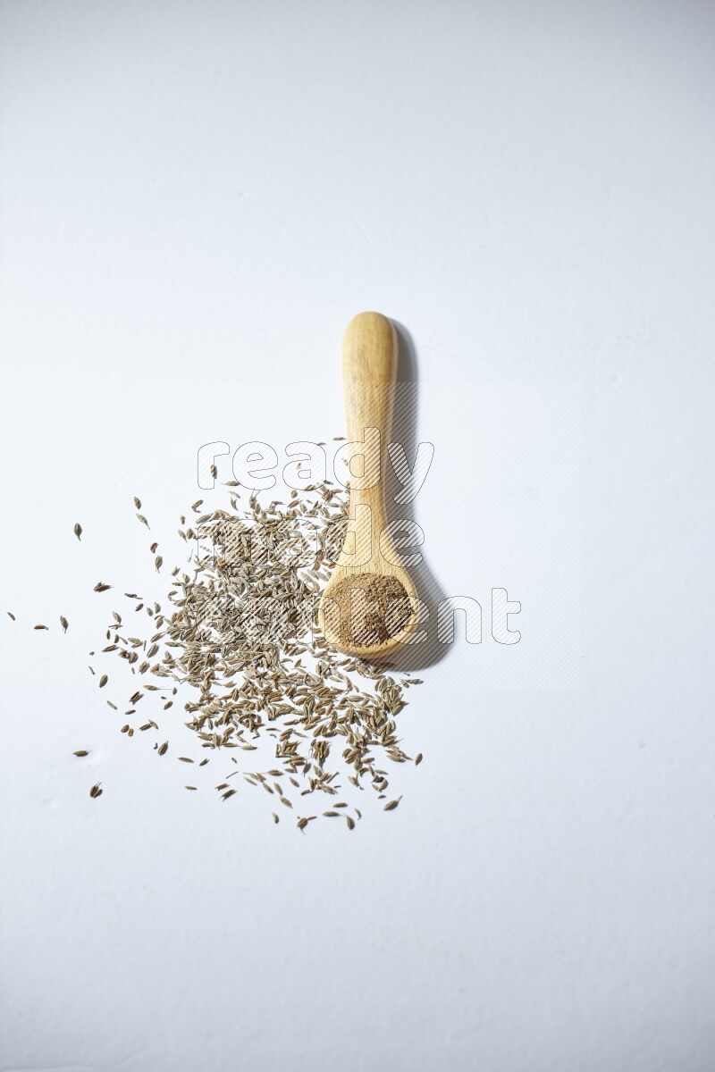 A wooden spoon full of cumin powder and cumin seeds beside it on white flooring