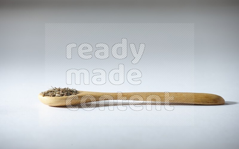A wooden spoon full of cumin seeds on a white flooring