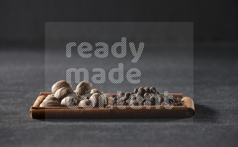 2 squares of cinnamon sticks full of nutmegs and allspice on black flooring