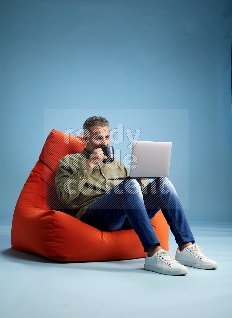 A man sitting on an orange beanbag and working on laptop