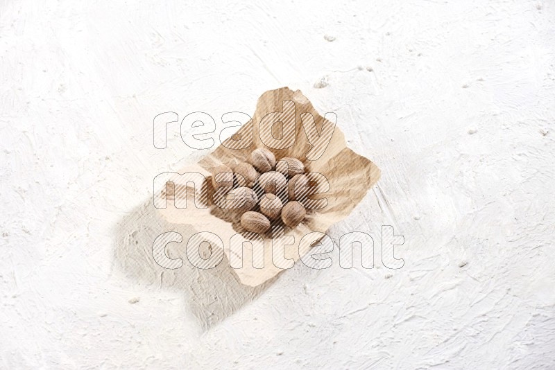 A crumpled piece of paper full of whole nutmeg seeds on a textured white flooring