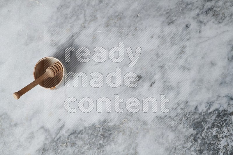 Multicolored Pottery Bowl with wooden honey handle in it, on grey marble flooring, Top View