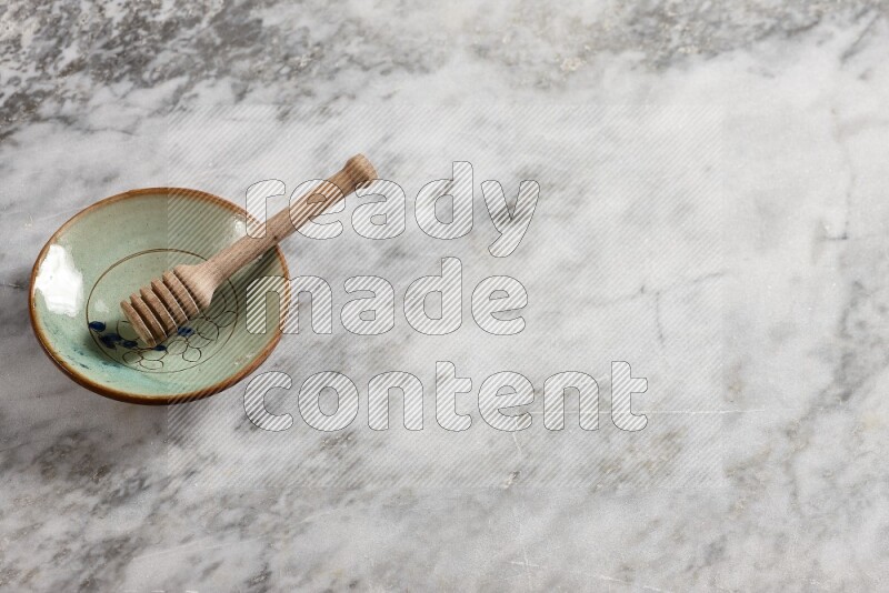 Decorative pottery plate with wooden honey dipper in it on grey marble background