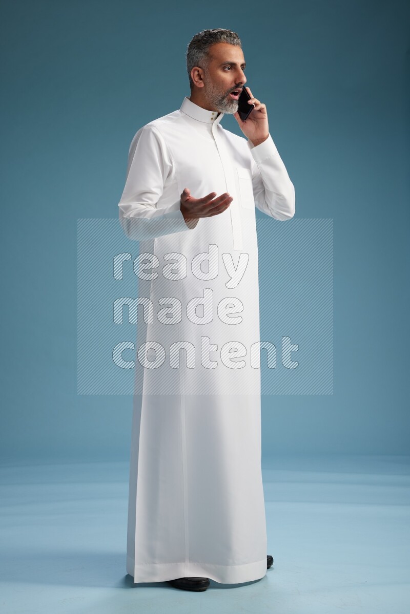 Saudi man wearing thob talking on the phone on blue background