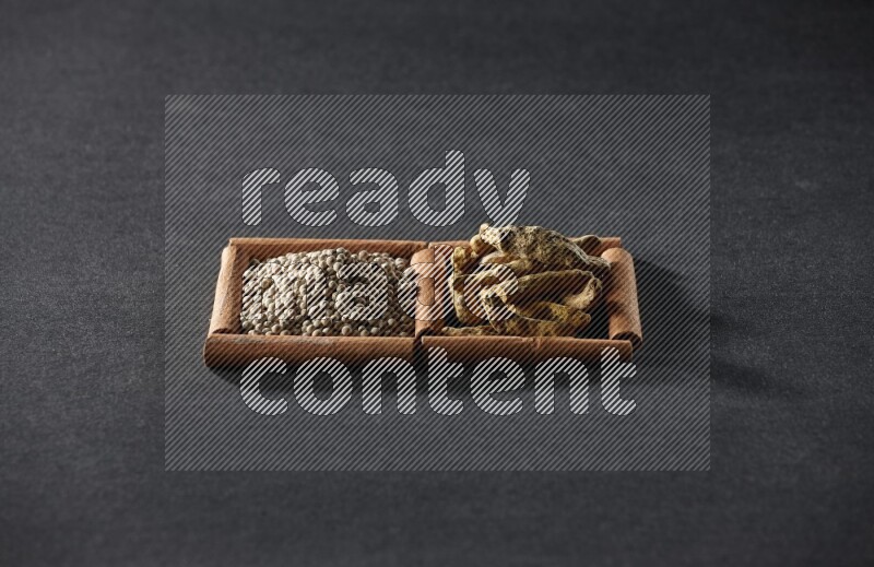 مربعان من أعواد القرفة ممتلئان بحبوب الفلفل الأبيض وأصابع الكركم علي خلفية سوداء