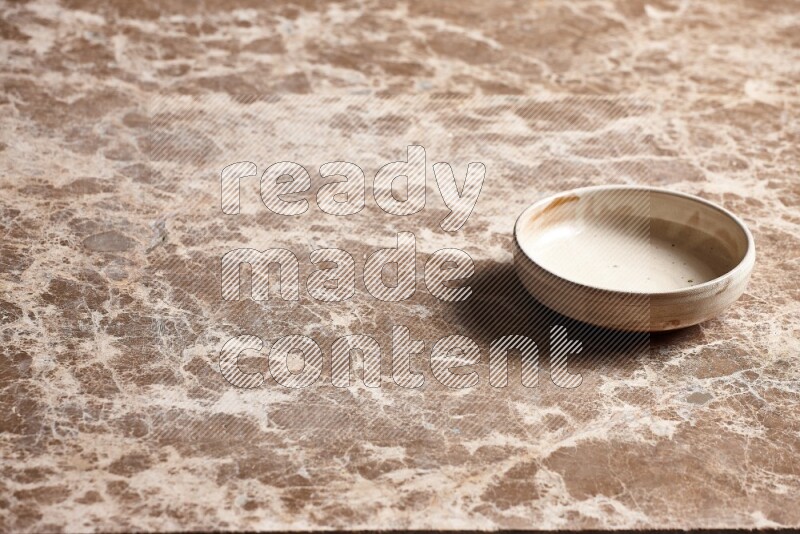 A beige pottery bowl on beige marble background