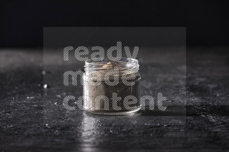 A glass jar full of black pepper powder on a textured black flooring